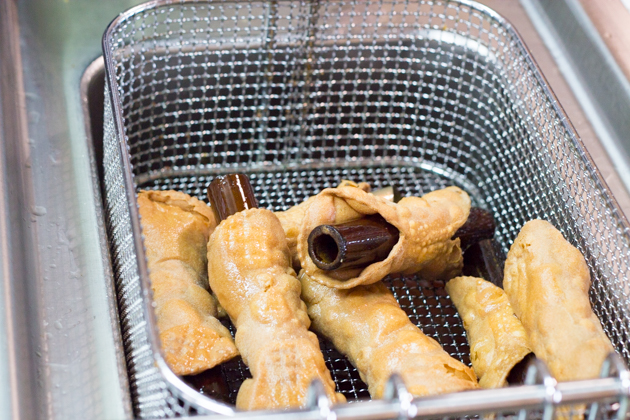 Frying the cannoli pastries with traditional wooden moulds 